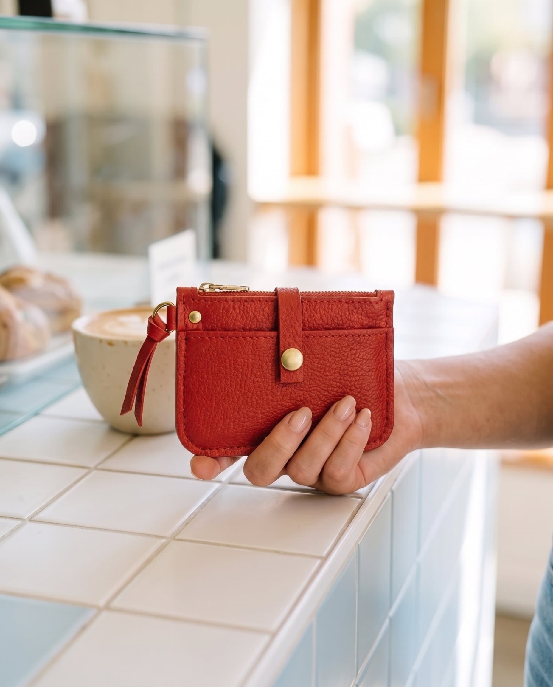 The Pocket Zip in Scarlet, in hand at a coffee counter